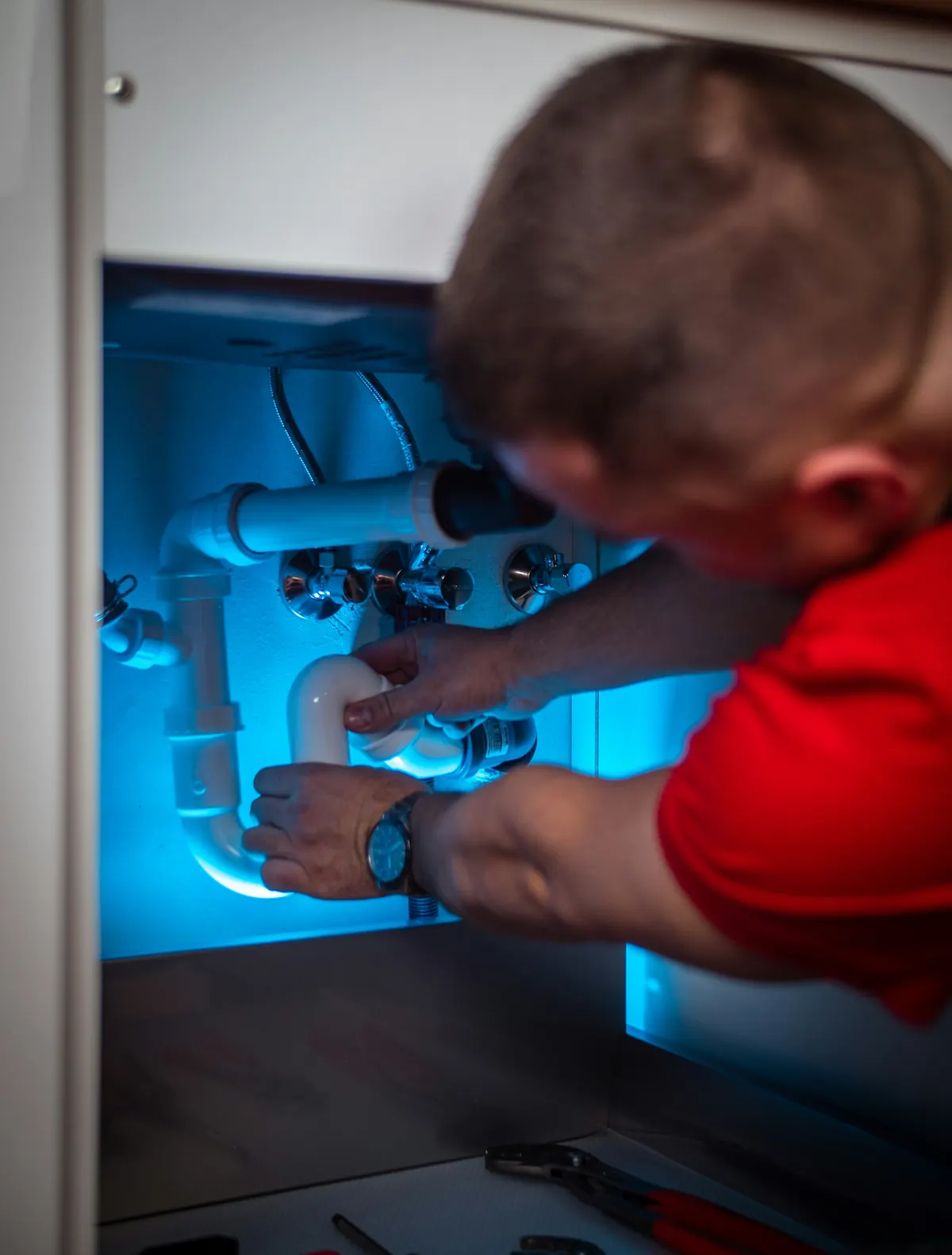 Plumber tightening a pipe connection in a cabinet