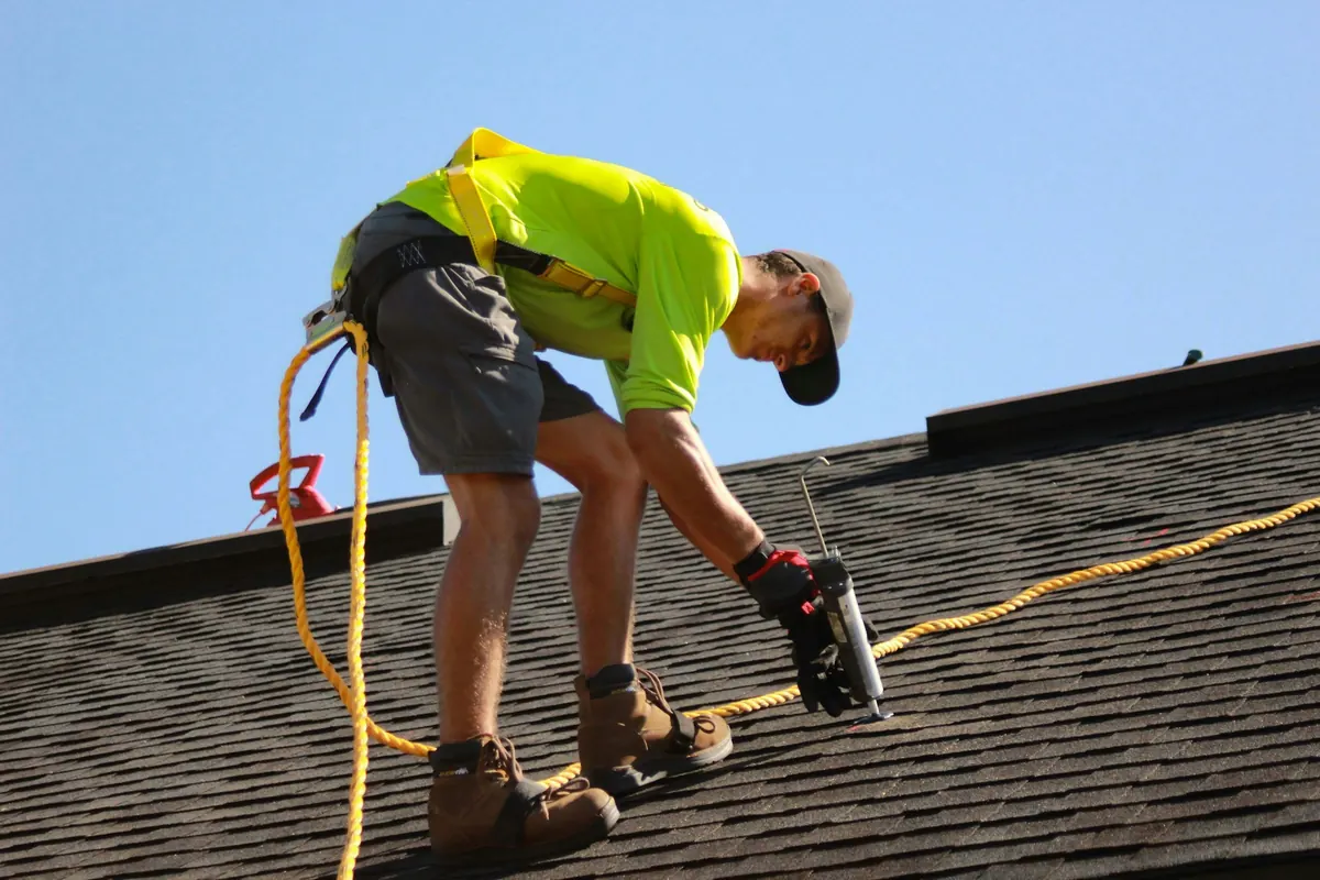 Roofer fastening shingles with a power drill